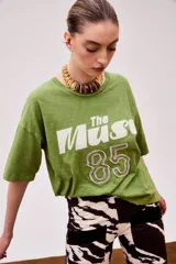 Remera verde con estampado frontal con la frase "The Muse" y el número 85 en blanco y lila. De corte holgado y largo a la cadera.