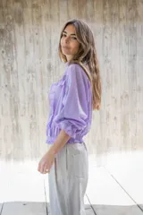 Blusa lila de cuello alto y manga 3/4 con elástico en el bajo. Presenta volados verticales en el frente.