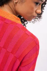 Saco de punto con diseño de bloques de color en tonos rojos y fucsias, con terminaciones en color naranja. Presenta cuello redondo, cierre frontal con botones y mangas largas.