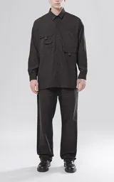 Camisa de manga larga color negro, estilo técnica con calce oversize. Presenta múltiples bolsillos frontales con solapa y detalle de tiras, un pequeño bordado de tijeras en el pecho izquierdo y botones en la cartera frontal y puños.