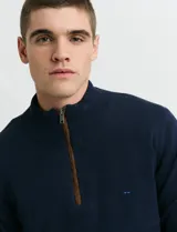 Sweater de punto color verde oliva, con cuello alto y medio cierre frontal. Presenta coderas en símil nappa y puños acanalados.