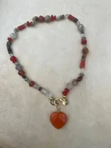 Collar con dije de corazón facetado en color verde esmeralda, con cadena de cuentas de cristal facetadas en tonos amarillos y dorados.