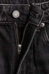 Jean de tiro alto con corte wide leg, confeccionado en denim rígido de color negro con efecto lavado. Presenta diseño clásico de cinco bolsillos, cierre frontal con cremallera y botón, y terminación de botamanga con ruedo desflecado.