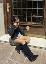 Bota alta de gamuza negra con caña alta, flecos laterales, tiras con hebillas metálicas en el tobillo y taco cuadrado.