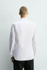 Camisa slim fit de algodón con cuello smoking, manga larga con puño doble para gemelos y pechera combinada a tono con cierre frontal de botones.