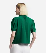 Blusa verde esmeralda de crepé con cuello alto con botones dobles y pequeña abertura abajo y mangas cortas abullonadas con botones.