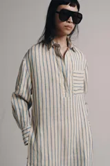 Vestido midi estilo camisero de Zara Woman Collection, confeccionado en lino, con estampado de rayas verticales azules sobre fondo beige. Cuenta con cuello solapa, escote en V con botonadura parcial, manga larga con puños abotonados, un bolsillo de plastrón en el pecho y bajo redondeado.