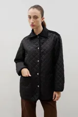 Campera acolchada de diseño capitoneado en color negro, con cuello camisero de pana, cierre frontal mediante botones metálicos a presión y bolsillos frontales amplios.