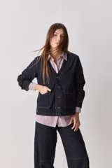 Sobrecamisa de jean azul oscuro, de calce relajado, escote en V, bolsillos delanteros aplicados, cierre frontal con botones metálicos y pespuntes en contraste.