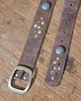 Cinto de cuero marrón con hebilla metálica dorada y detalle de tachas decorativas en tonos dorados y plateados.