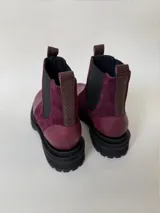 Botas tipo chelsea de cuero, combinando texturas en color bordó. Presentan paneles laterales elásticos en negro, suela track robusta y tiradores en la parte superior.