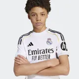 Camiseta de fútbol Adidas del Real Madrid, primera equipación temporada 25/26. Diseño en color blanco con detalles en negro y líneas amarillas sutiles, cuello redondo y mangas cortas. Incluye el escudo del club bordado y el logo de la marca.