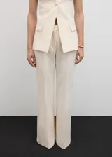 Pantalón de vestir color crema, de corte recto y diseño acampanado, con trabillas en la cintura, bolsillos laterales y cierre oculto.