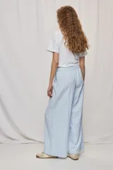 Pantalón de tiro alto con silueta amplia y caída fluida, confeccionado en tejido celeste con textura a rayas finas. Cuenta con cintura elástica con lazo de ajuste y bolsillos laterales.