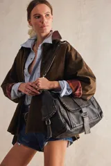 Cartera hobo de cuero color marrón oscuro con acabado gastado. Presenta una solapa frontal con detalles de ojales metálicos, una argolla metálica en la correa para el hombro y bolsillos laterales. Incluye un llavero colgante con candado y dijes.