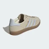 Championes Adidas Gazelle Indoor de gamuza color beige con las icónicas tres tiras en celeste claro. Presenta suela de caucho traslúcido y detalles en dorado.