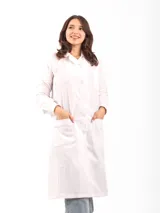 Túnica blanca de dama con cuello camisero, abotonada al frente, con dos bolsillos frontales con detalle de puntilla y pinzas verticales.