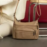 Bandolera de símil cuero color beige, con diseño de múltiples compartimentos. Cuenta con dos bolsillos frontales con cierre, doble apertura superior con cierre y un bolsillo trasero con cierre. Incluye correa larga regulable de cinta tejida.