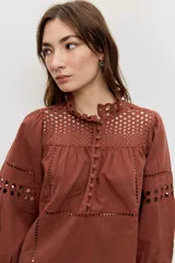 Camisa de manga larga abullonada color marrón, con detalles de bordados calados en el pecho y las mangas, y cierre frontal con botones.
