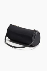 Cartera cilíndrica pequeña color negro con cierre superior y correa de hombro.