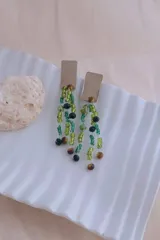 Caravanas colgantes de alpaca con placa rectangular superior y múltiples tiras de cuentas de cristal en tonos verdes y marrones.