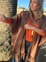 Capa estilo ruana marrón oscuro con flecos en el ruedo inferior, de diseño abierto y corte amplio.