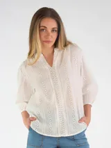 Blusa de broderie blanca con escote en V, mangas tres cuartos abullonadas y diseño holgado.