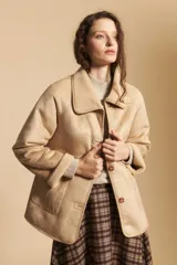 Gamulán de piel sintética en color beige, con interior de corderito, cuello amplio, cierre frontal con botones y bolsillos laterales.