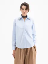Camisa de algodón con lycra en color celeste claro, de corte clásico y manga larga. Presenta apliques de piedras de cristal en las puntas del cuello y una cartera oculta con botones.
