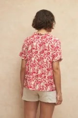 Blusa blanca con finas rayas verticales negras, de manga corta con volados y escote en V con pequeños botones y detalle de volado en el borde.