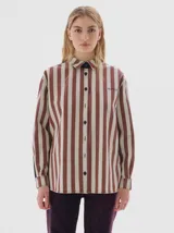 Camisa de denim con estampado de rayas verticales en tonos bordó y crema. Presenta cuello clásico, cierre frontal con botones negros, canesú trasero negro y paneles laterales negros en las mangas. Incluye un pequeño bordado con el nombre de la marca en el pecho.