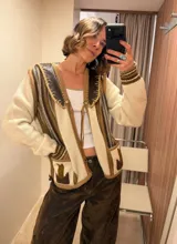 Cardigan tejido de punto en tonos crudo, beige y marrón, con detalles de cuero en el cuello y bolsillos frontales. Presenta diseño rayado, mangas largas y cierre con botones y lazo.