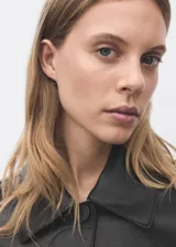 Chaqueta corta de efecto piel en color negro, con cuello de solapa, cierre frontal de botones y dos bolsillos de parche con solapa en la parte delantera. Presenta un diseño recto y forro interior.