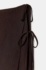 Conjunto de pantalón ancho marrón oscuro con una sobrefalda envolvente (tipo pareo o falda cruzada) que se ata con lazadas finas en el lateral.