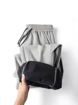 Pantalón deportivo negro de corte ancho y tiro alto con cordón ajustable en la cintura. Presenta tres franjas verticales grises oscuras en los laterales y un bolsillo cargo con solapa en el muslo derecho. Los tobillos son ajustables.
