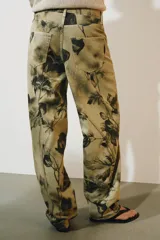 Pantalón jeans ZW Collection de tiro medio y corte balloon, confeccionado en algodón con diseño estampado de flores en tonos oscuros sobre base beige. Cuenta con cinco bolsillos, trabillas para cinto y cierre frontal con cremallera y botón metálico.