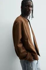 Cazadora bomber negra de corte regular fit, confeccionada en tejido efecto ante. Cuenta con cuello, puños y bajo en rib elástico, manga larga, bolsillos de vivo en la cadera y un bolsillo interior. Cierre frontal con cremallera.