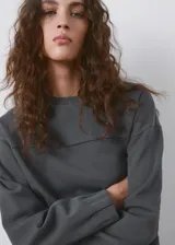 Buzo gris oscuro de piqué, de cuello redondo y manga larga con puños ajustados, con detalle de costura horizontal en el pecho.