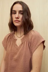 Blusa color rosado con textura arrugada, escote en V con detalle de fruncido y mangas cortas.