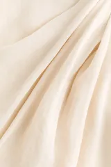 Vestido corto sin mangas de color beige con un leve brillo, corte entallado, elegante escote bote y tiras anchas para atar en un hombro y en el lado opuesto de la cintura. Cuenta con cierre oculto en un lateral.