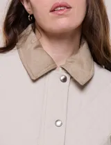 Campera acolchada capitoneada, marca Michael Kors, de color beige con cuello camisero de gamuza en contraste. Cuenta con cierre frontal de botones a presión metálicos, bolsillos laterales inclinados con ribetes de gamuza y mangas largas.