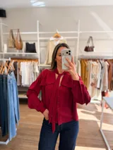 Camisa de color rojo intenso con volados en los hombros y lazo ajustable en el cuello. Presenta un cierre frontal con botones y un diseño de calce amplio.