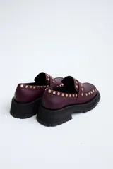 Mocasines de cuero color marrón con suela track negra y tachas doradas.