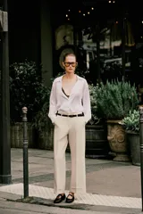 Pantalón de vestir color beige, tiro alto, corte ancho y pierna recta. Presenta un bajo con vuelta y viene acompañado de un cinturón fino de cuero marrón con hebilla metálica.