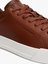 Zapatillas de estilo tenis Tommy Hilfiger confeccionadas en piel color marrón, con diseño de corte bajo, cordones al tono y suela de goma blanca. Presenta un panel de gamuza a contraste en el talón y el logo de la marca grabado en el lateral.
