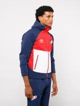 Campera deportiva Umbro del Club Nacional de Football, modelo Summit. Presenta un diseño con bloques de color en azul, rojo y blanco, con capucha, cierre frontal y bolsillos laterales con cierre. Incluye el logo de la marca y el escudo del club en el pecho.