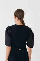 Top tejido negro con escote recto y mangas balloon de poplín. Tiene tiras tejidas para ajustar en la cintura.