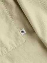 Camisa de manga larga color beige claro, con cierre frontal de botones, doble bolsillo en el pecho y logo pequeño en uno de los bolsillos.