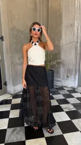 Falda larga de encaje negro con diseño de capas, presentando una sección superior opaca y una sección inferior transparente con terminación de volado en el ruedo.