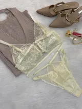 Conjunto de lencería de encaje color champagne, compuesto por un bralette estilo top con cierre frontal de gancho y breteles regulables, y una tanga de tiro alto con tiras laterales ajustables.